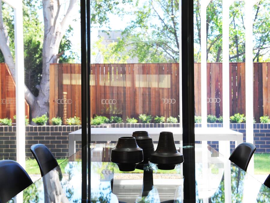 A dining area with a glass table and chairs, a wooden fence, and a brick wall in the background.