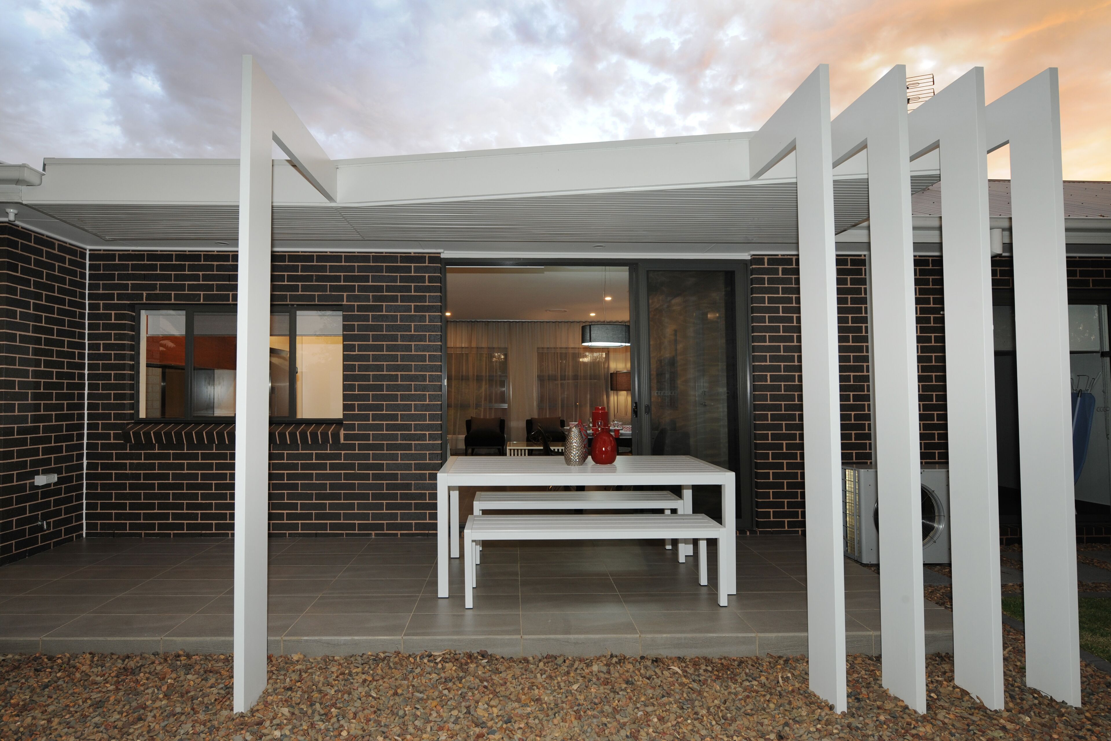 A modern building with a brick exterior, a white table and bench in the foreground, and a glass door leading to an interior space.