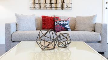 A modern living room with a grey sofa, two geometric metal sculptures on a glass coffee table, and patterned throw pillows.