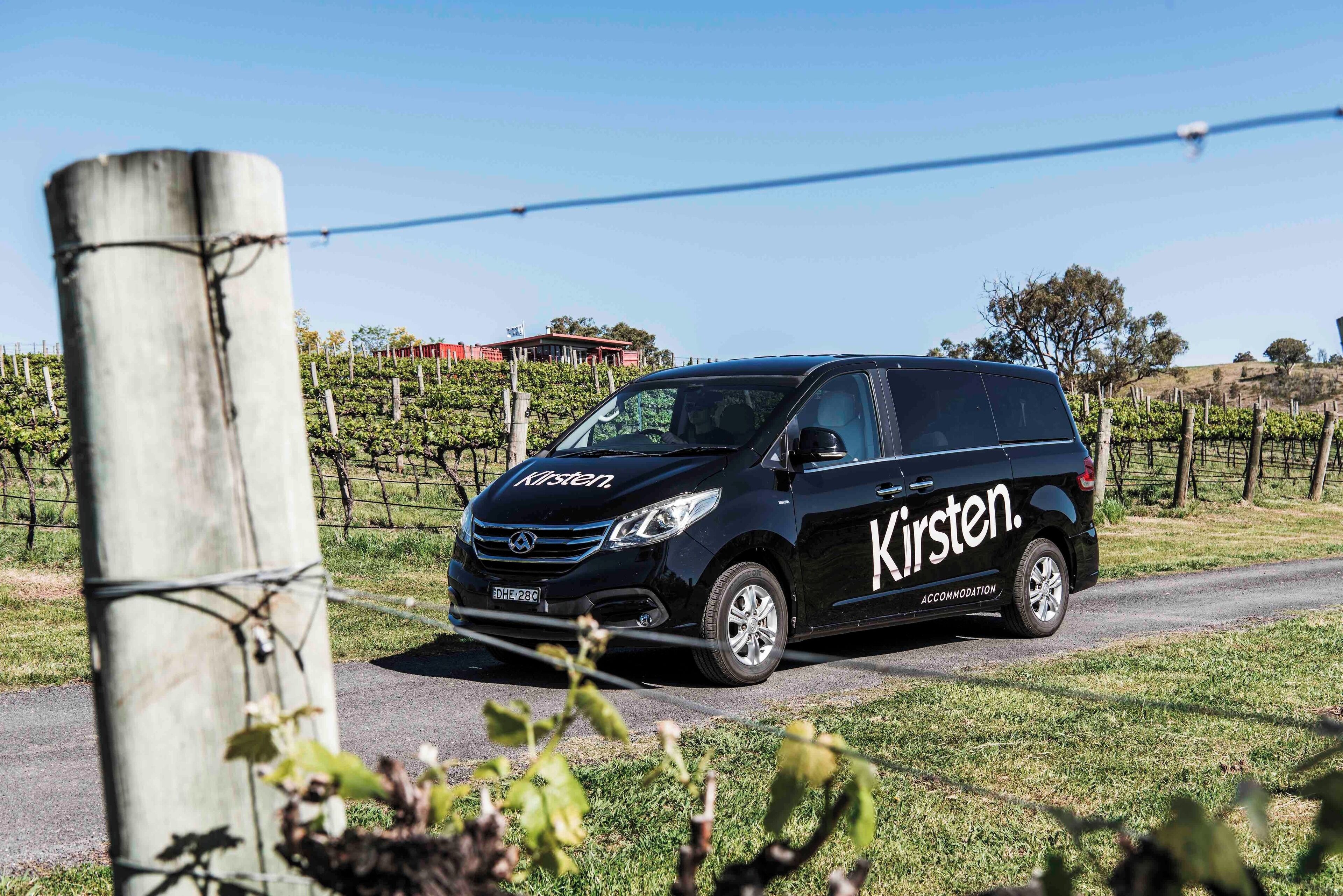 Una minivan negra con la marca 'Kirsten' estacionada en una carretera rural.