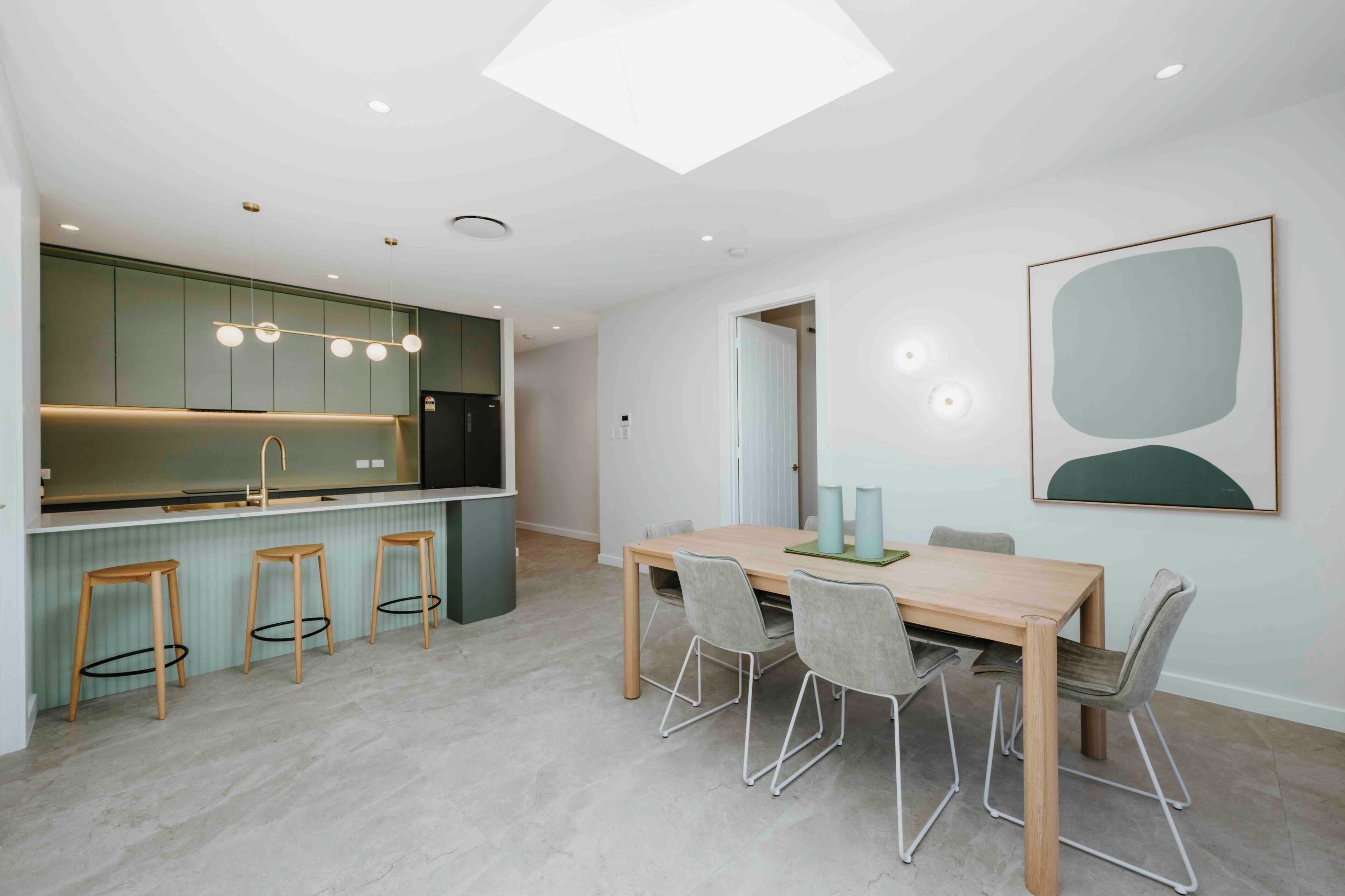 Una cocina moderna con una isla central, taburetes de bar y un comedor con una mesa y sillas de madera.