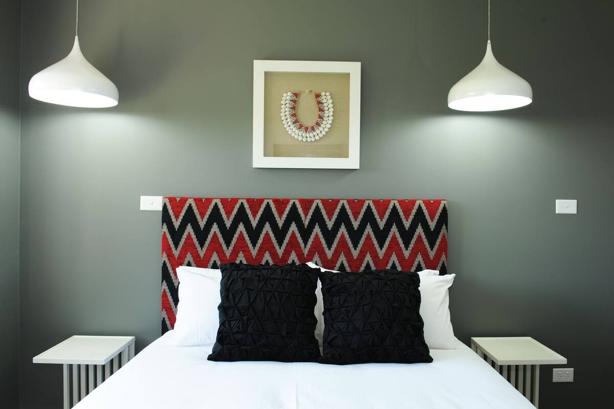 A neatly arranged hotel room with a bed, two bedside tables, a wall-mounted picture, and two pendant lights.