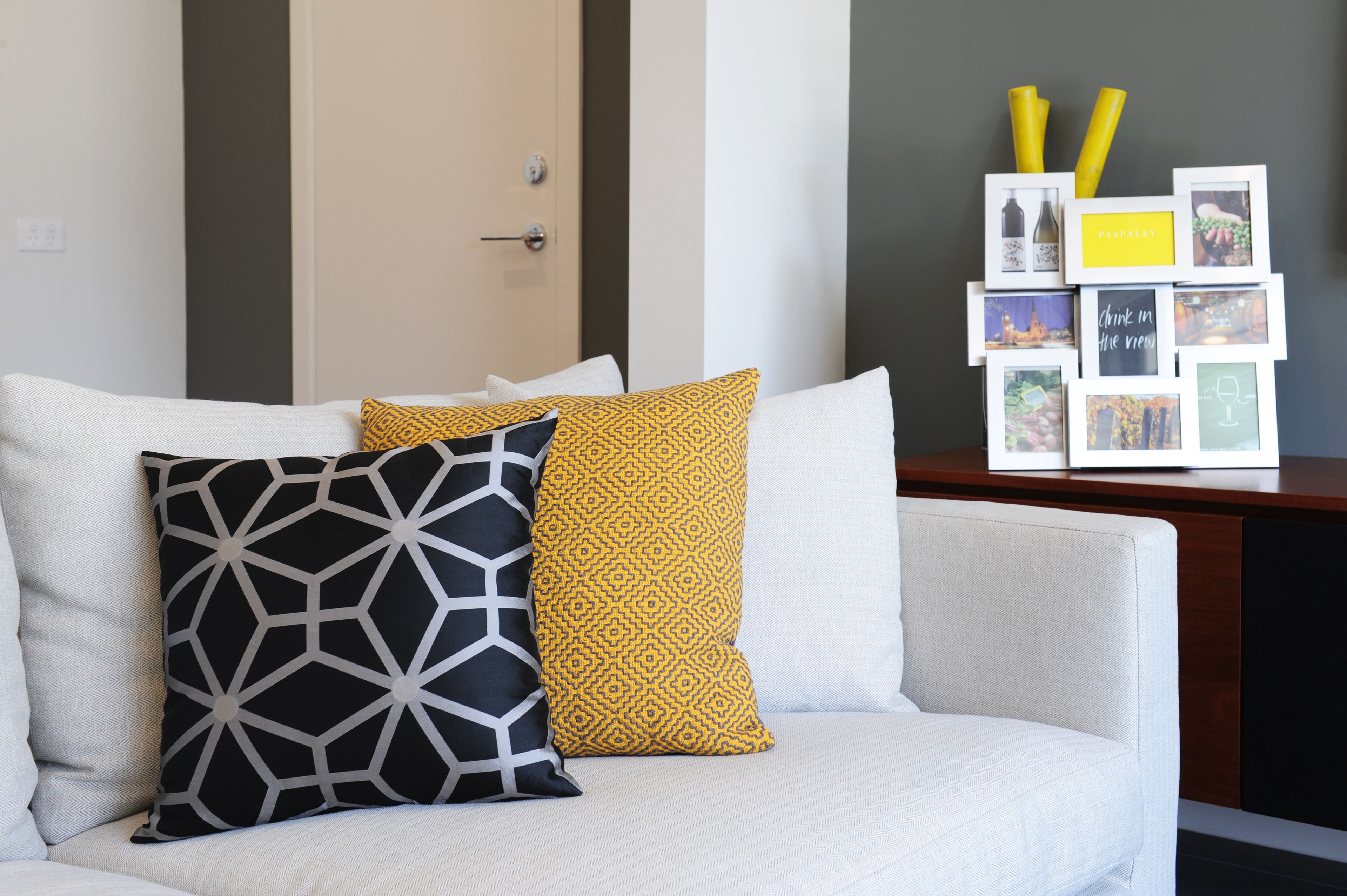 A modern living room with a white sofa, a geometric patterned pillow, and a yellow patterned pillow.