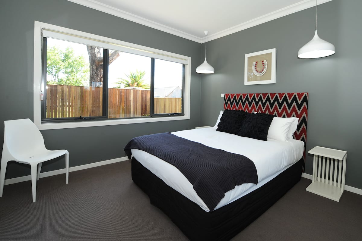 A bedroom with a large bed, a window, a chair, and a bedside table.