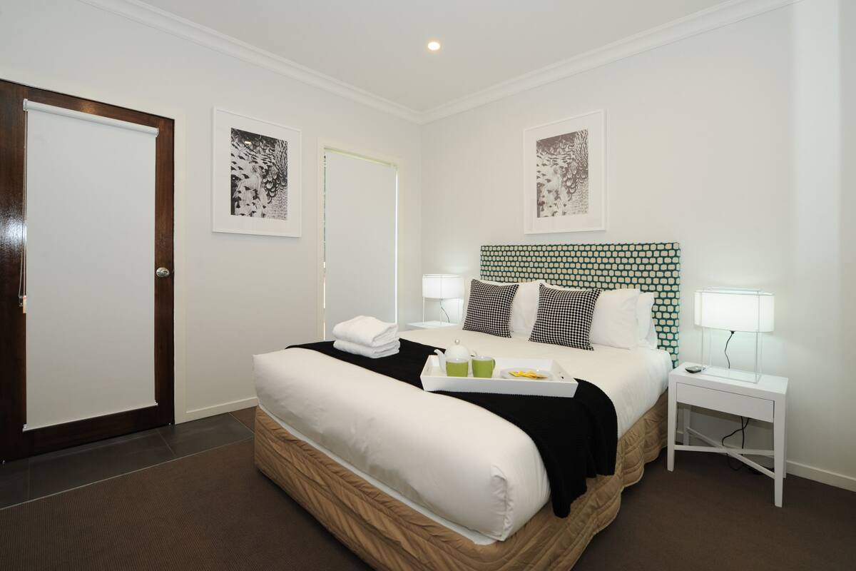 A hotel room with a large bed, a bedside table with a lamp, and artwork on the walls.