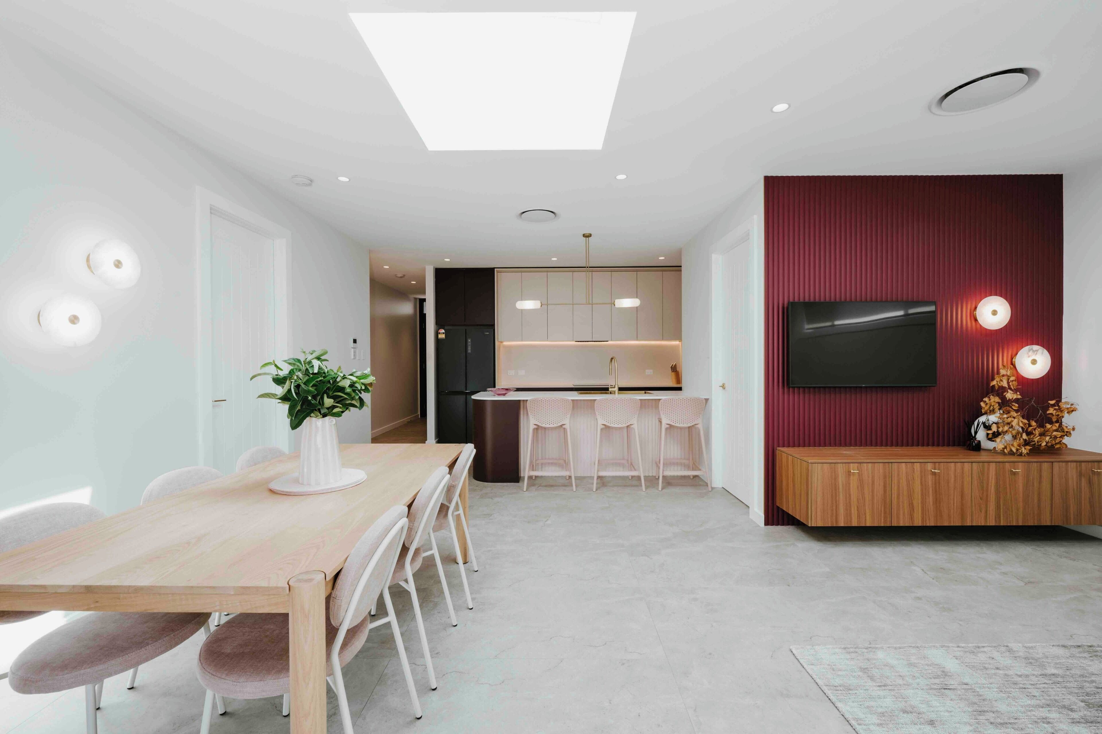 Una cocina moderna con una isla central, un comedor con mesa y sillas de madera, y un televisor montado en una pared roja.