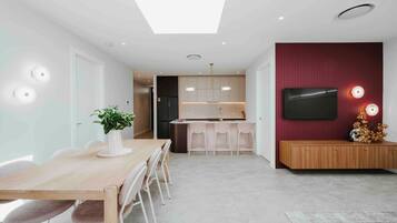 Una cocina moderna con una isla central, un comedor con mesa y sillas de madera, y un televisor montado en una pared roja.