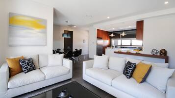 A modern living room with two white sofas, a coffee table, and a dining area in the background.