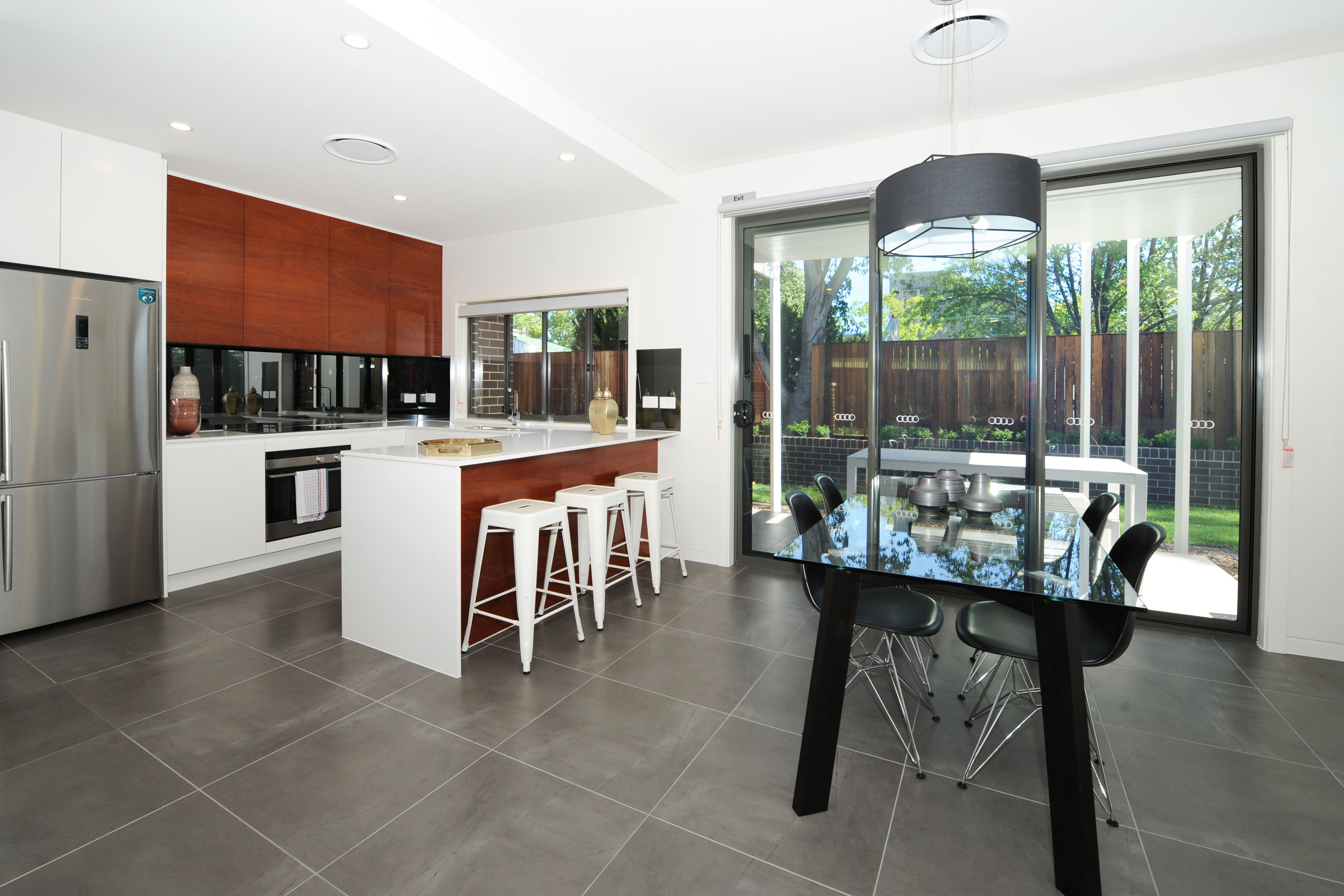 A modern kitchen with a central island, white bar stools, and a dining table with chairs.