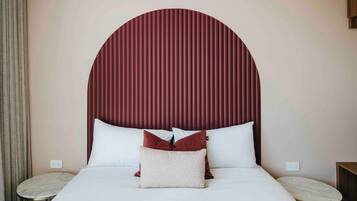 A neatly made bed with white bedding and two pillows, a round bedside table, and a wall-mounted power outlet.