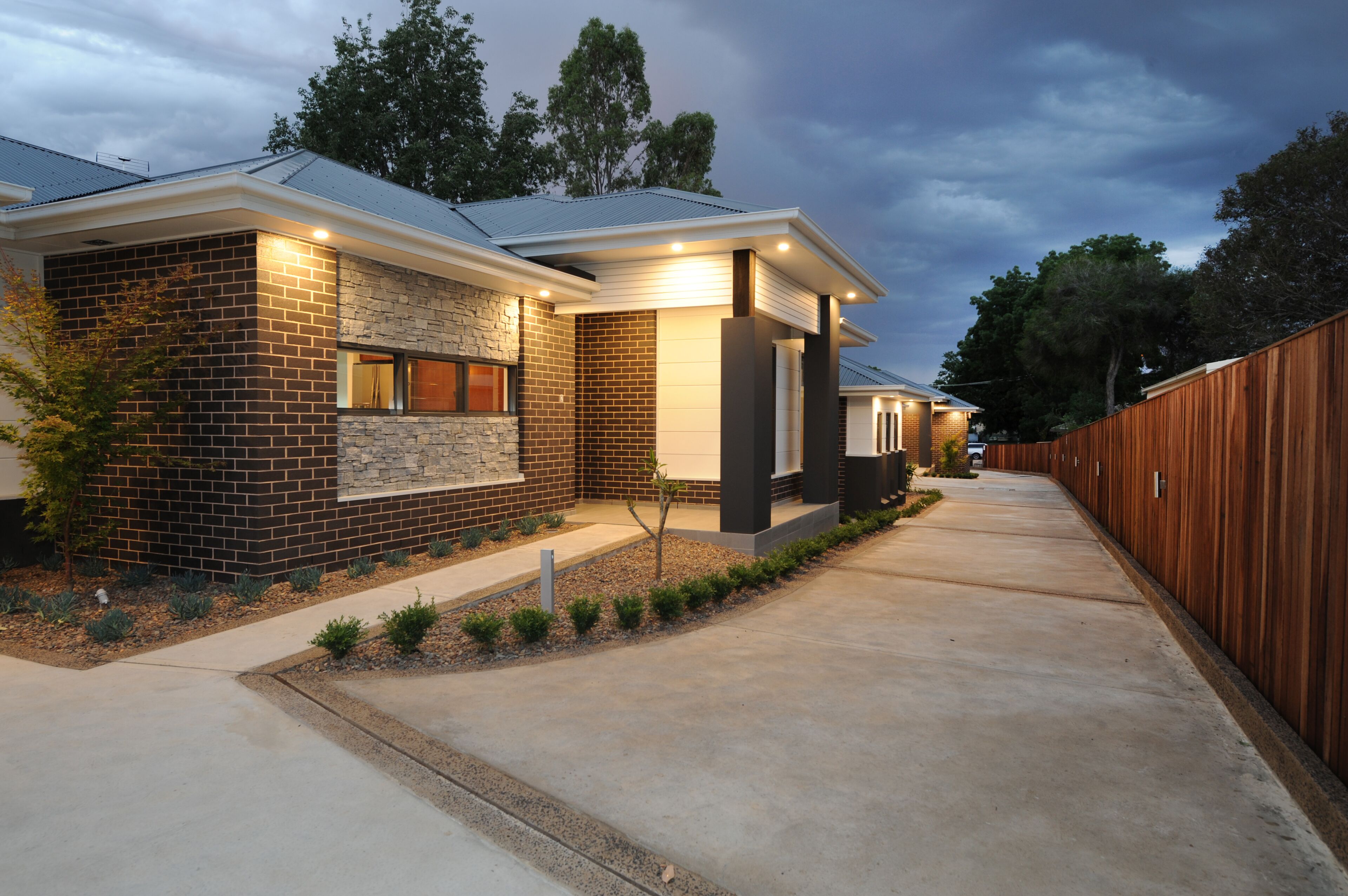 A modern two-story house with a brick exterior, a stone accent wall, and a wooden fence.