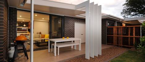 A modern outdoor patio with a white table and bench, a barbecue grill, and a brick wall.
