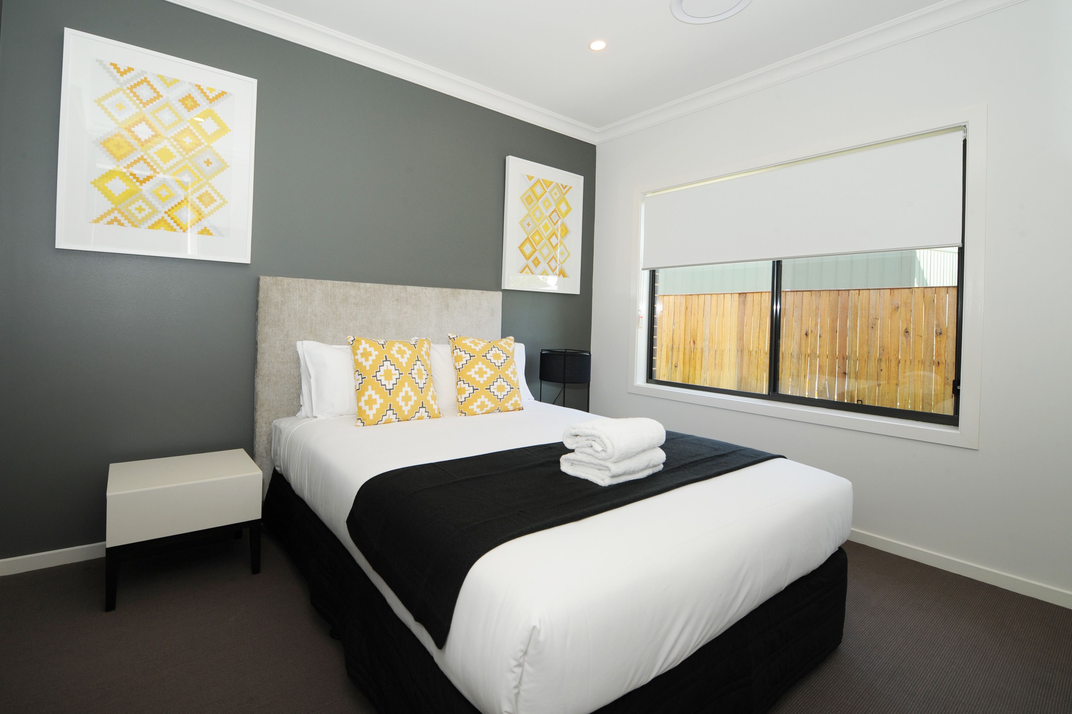A neatly arranged hotel room with a large bed, a bedside table, and two wall-mounted artworks.