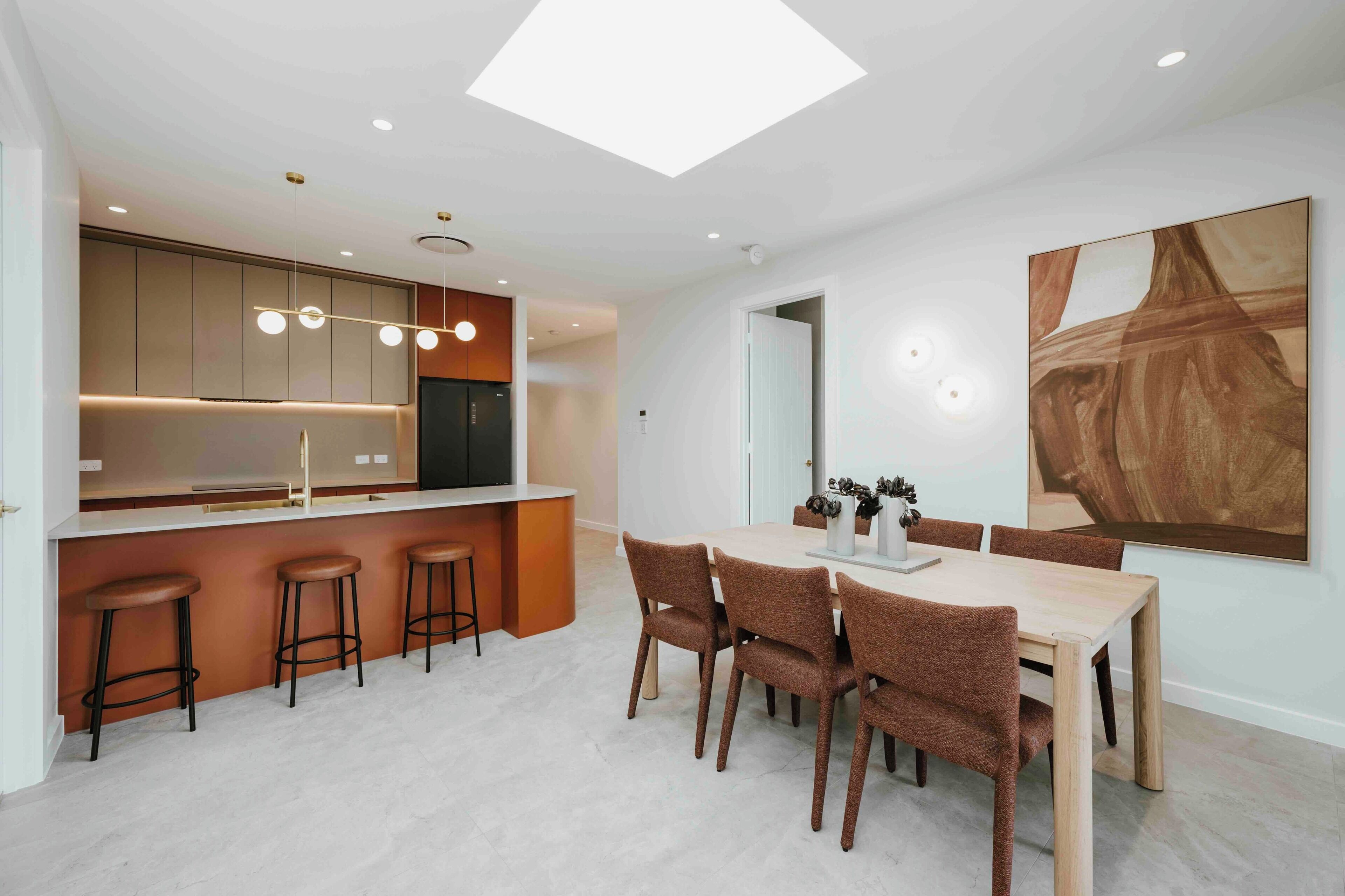 A modern kitchen with a central island, bar stools, and a dining area with a table and chairs.