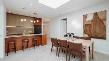 A modern kitchen with a central island, bar stools, and a dining area with a table and chairs.