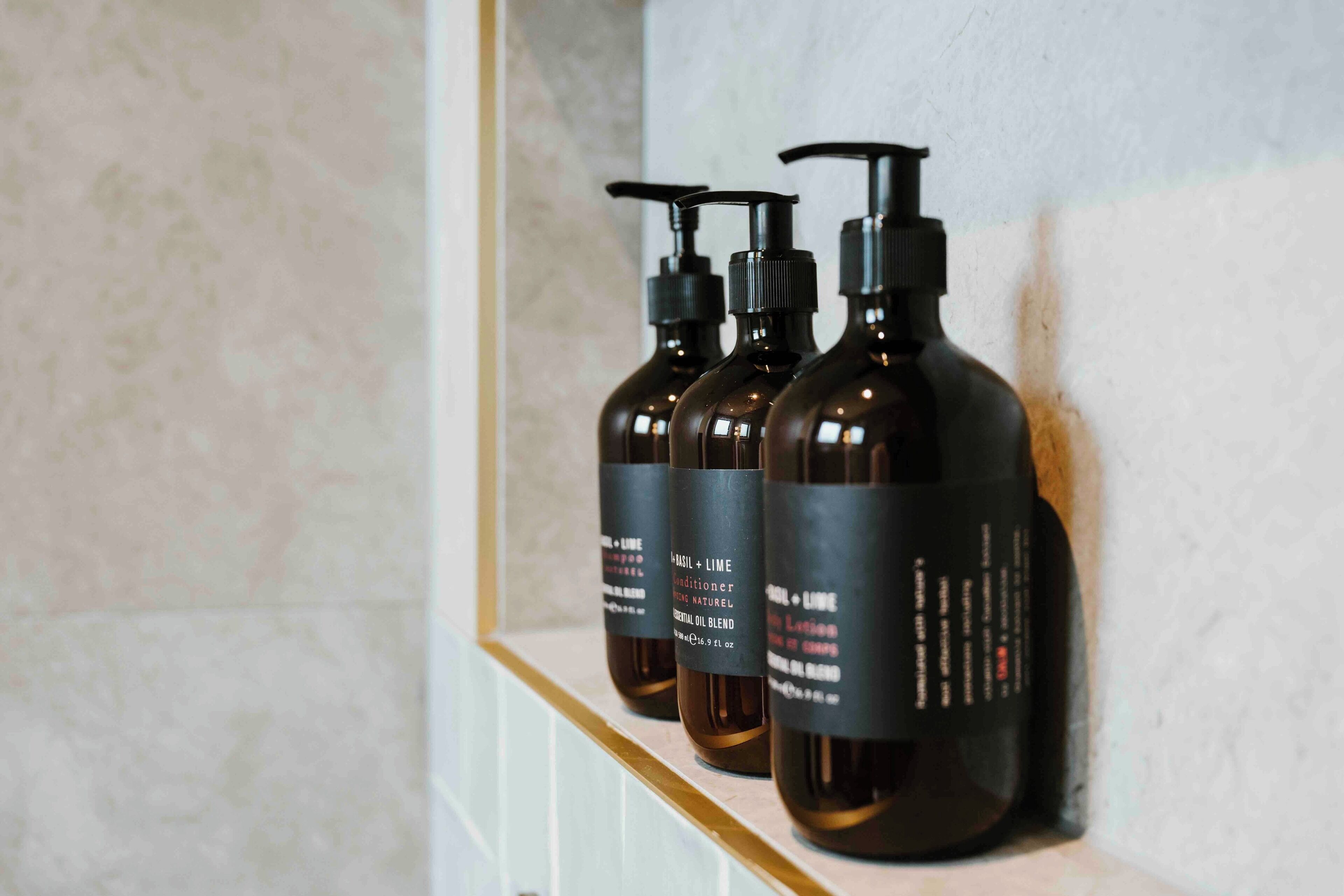 Three bottles of 'Basil + Lime' conditioner on a shelf.