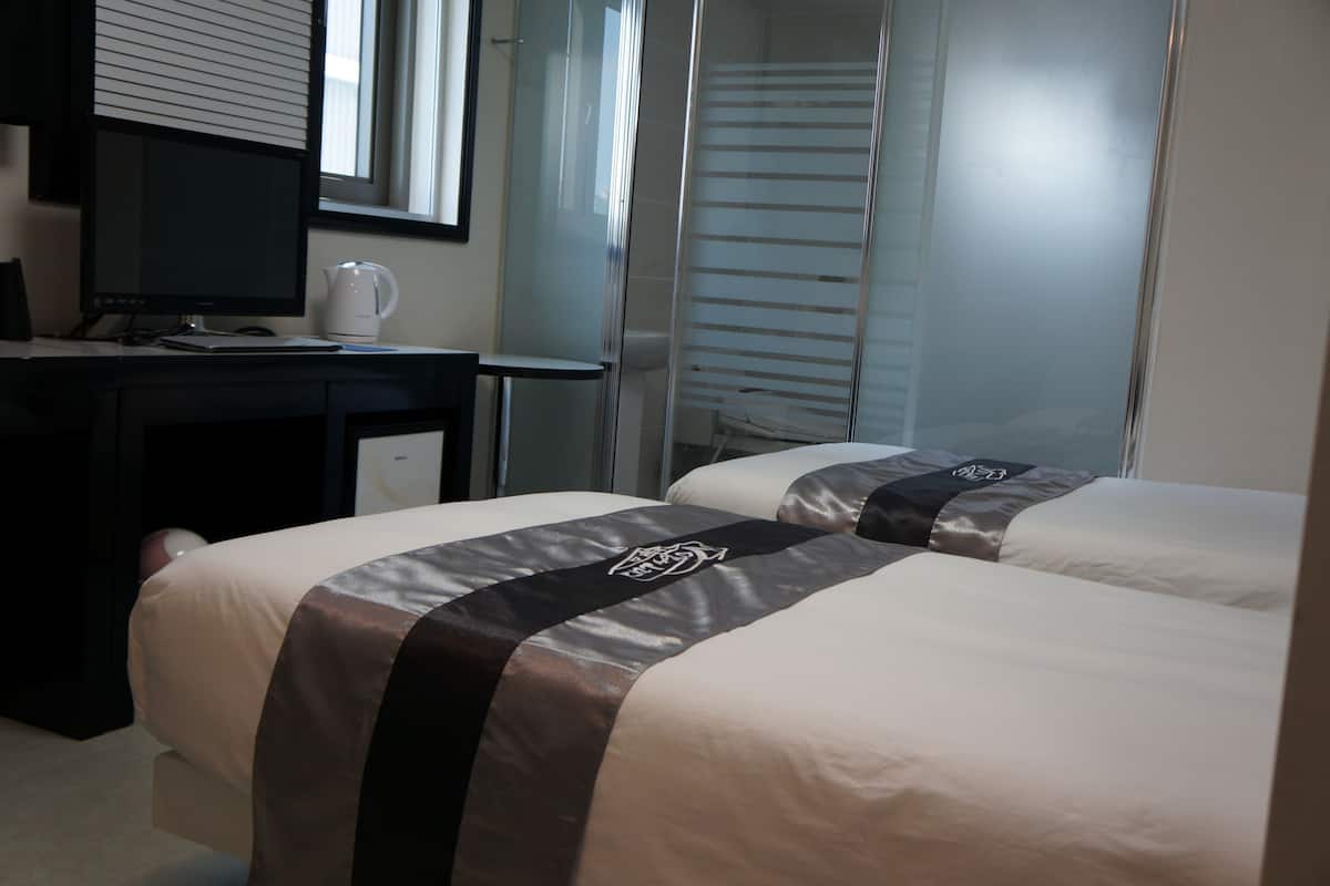A hotel room with two beds, a desk with a computer, a coffee maker, and a window with blinds.