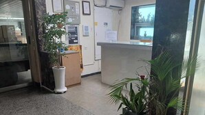 Un área de recepción con mostrador, una planta en maceta y un tablón de anuncios.