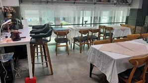 Un comedor con mesas y sillas, una zona de cocina con electrodomésticos y ventanas amplias con cortinas.