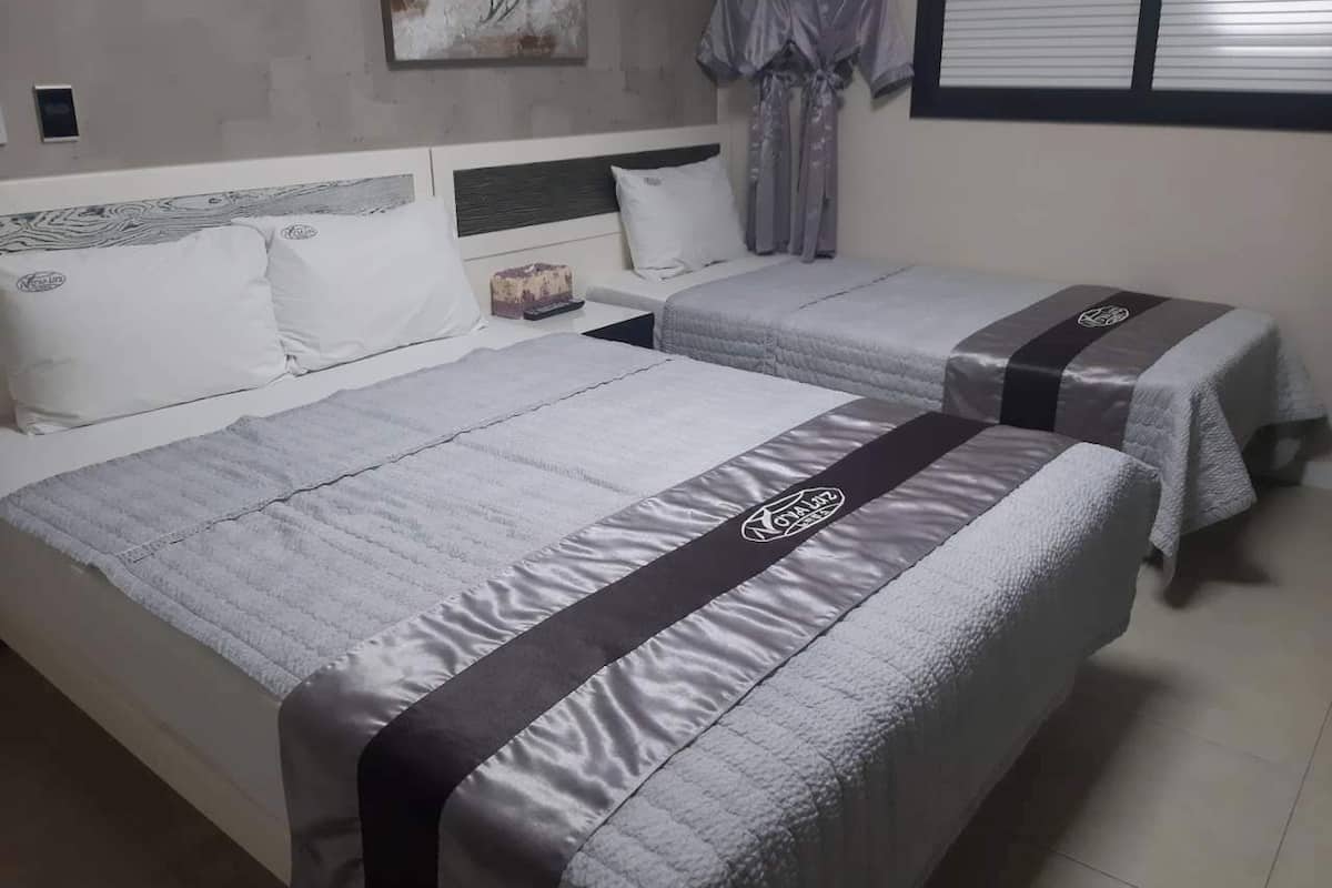 A hotel room with two beds, a headboard, a painting, and a window with blinds.