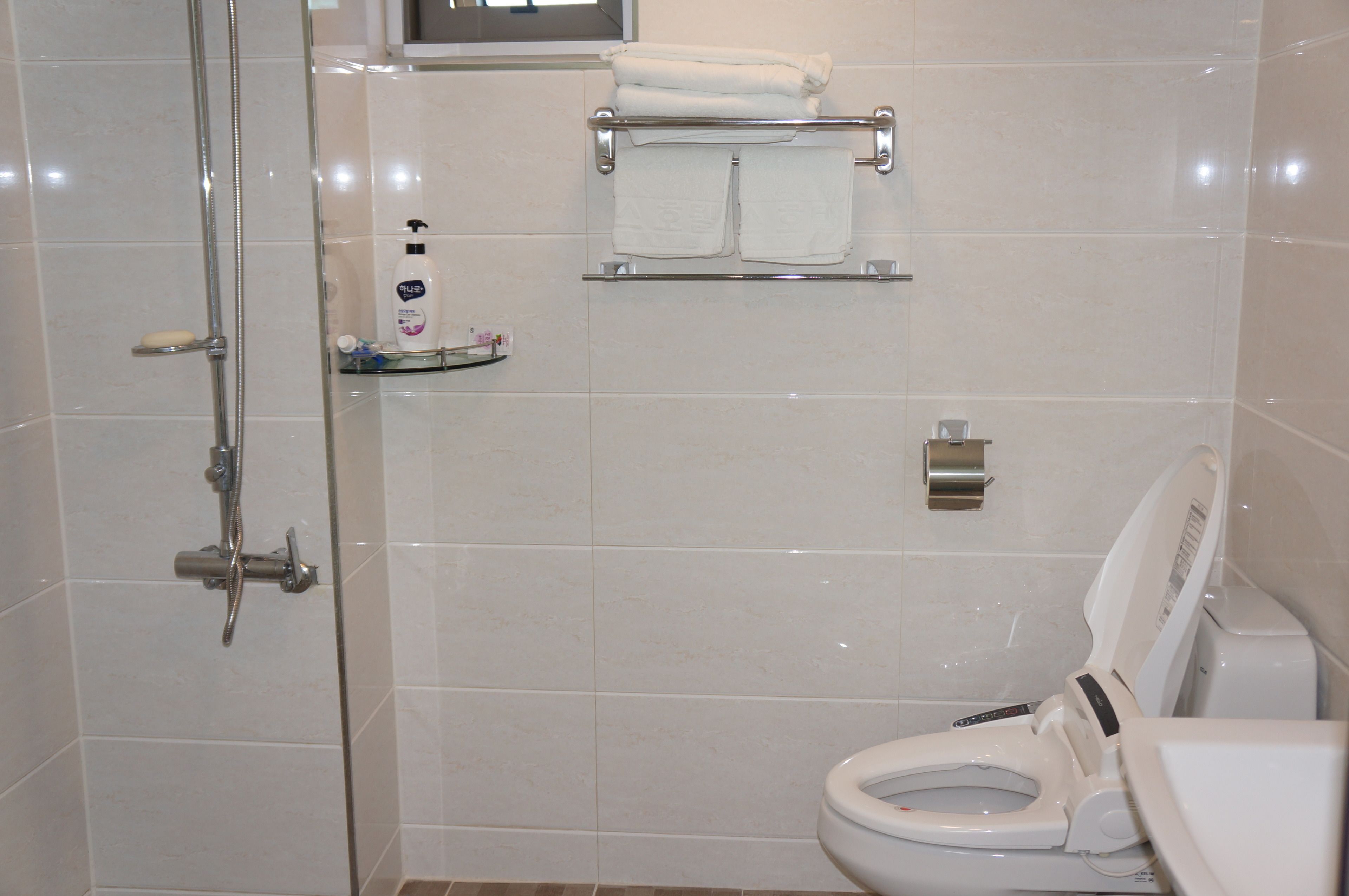 A modern bathroom with a glass-enclosed shower, a toilet with a bidet attachment, and a towel rack with folded towels.