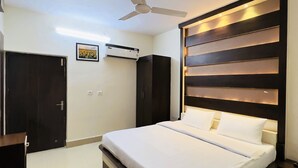 A modern bedroom with a bed, a ceiling fan, an air conditioning unit, and a dark wooden wardrobe.