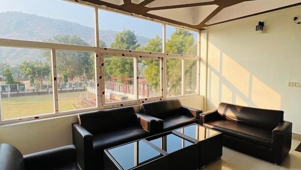 A modern lounge with black leather sofas and glass coffee tables, large windows offering a view of a playground and hills.