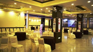 A banquet hall with rows of tables and chairs, decorative ceiling, and a large screen displaying a staircase.