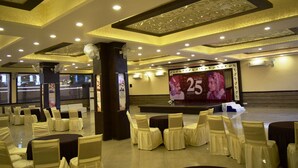 A banquet hall with rows of tables and chairs, a stage with a large screen, and decorative ceiling elements.