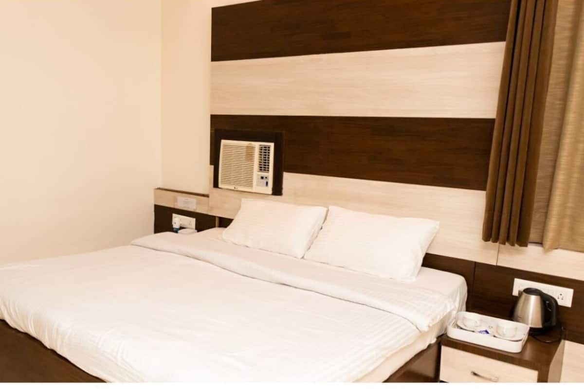 Ein Hotelzimmer mit einem großen Bett, einem Nachttisch mit Wasserkocher und einer Wand-Klimaanlage.