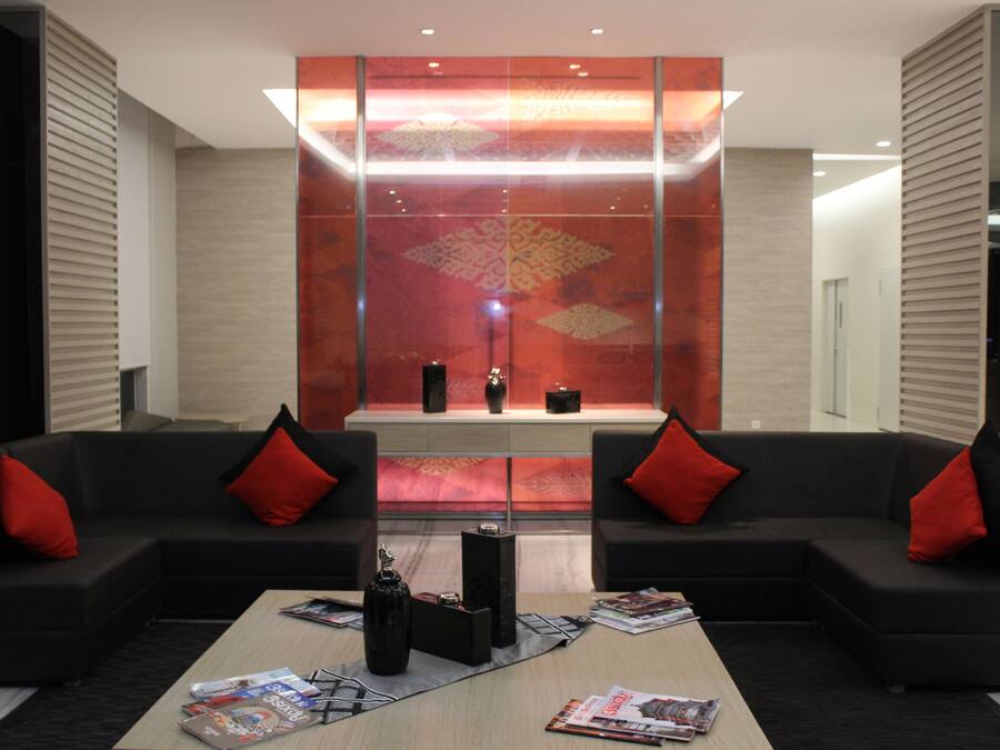 Un vestíbulo moderno con sofás negros, cojines rojos, un muro reflectante en el centro y revistas sobre la mesa de centro.