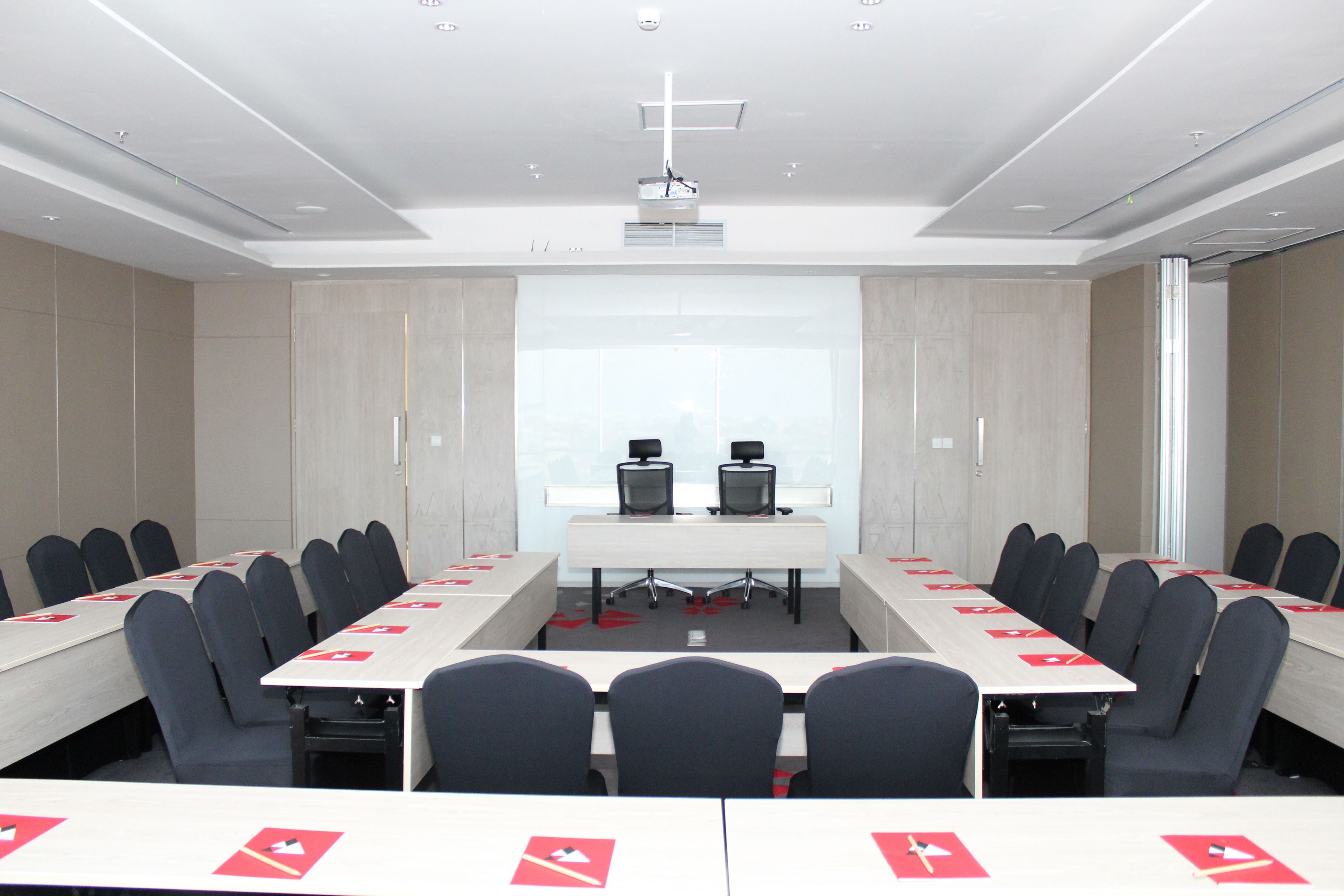 Un salón de conferencias con una mesa larga, múltiples sillas y una pantalla de proyector al frente.