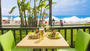 An outdoor dining area with a table set for two, overlooking a beach with umbrellas and people in the background. - Sandy Beach Hotel - All Inclusive (Manavgat)