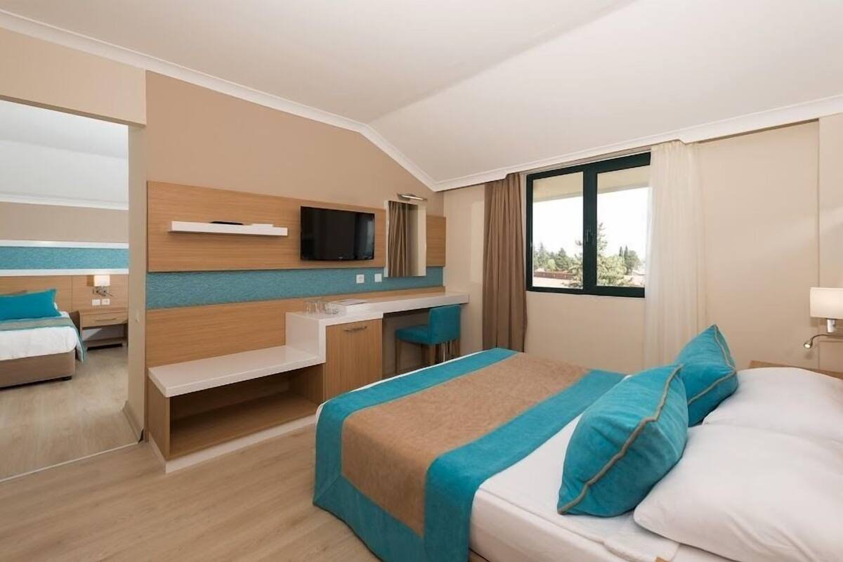 A hotel room with a bed, a desk, a TV mounted on the wall, and a window with curtains.