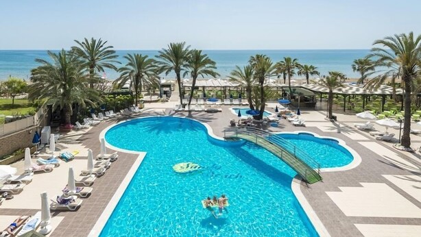 A swimming pool with a unique shape, surrounded by lounge chairs and umbrellas, with a view of the sea. - Sandy Beach Hotel - All Inclusive (Manavgat)