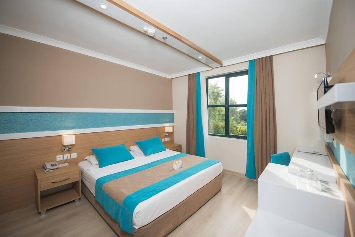 A hotel room with a large bed, a desk, a chair, a TV, and a window with curtains.