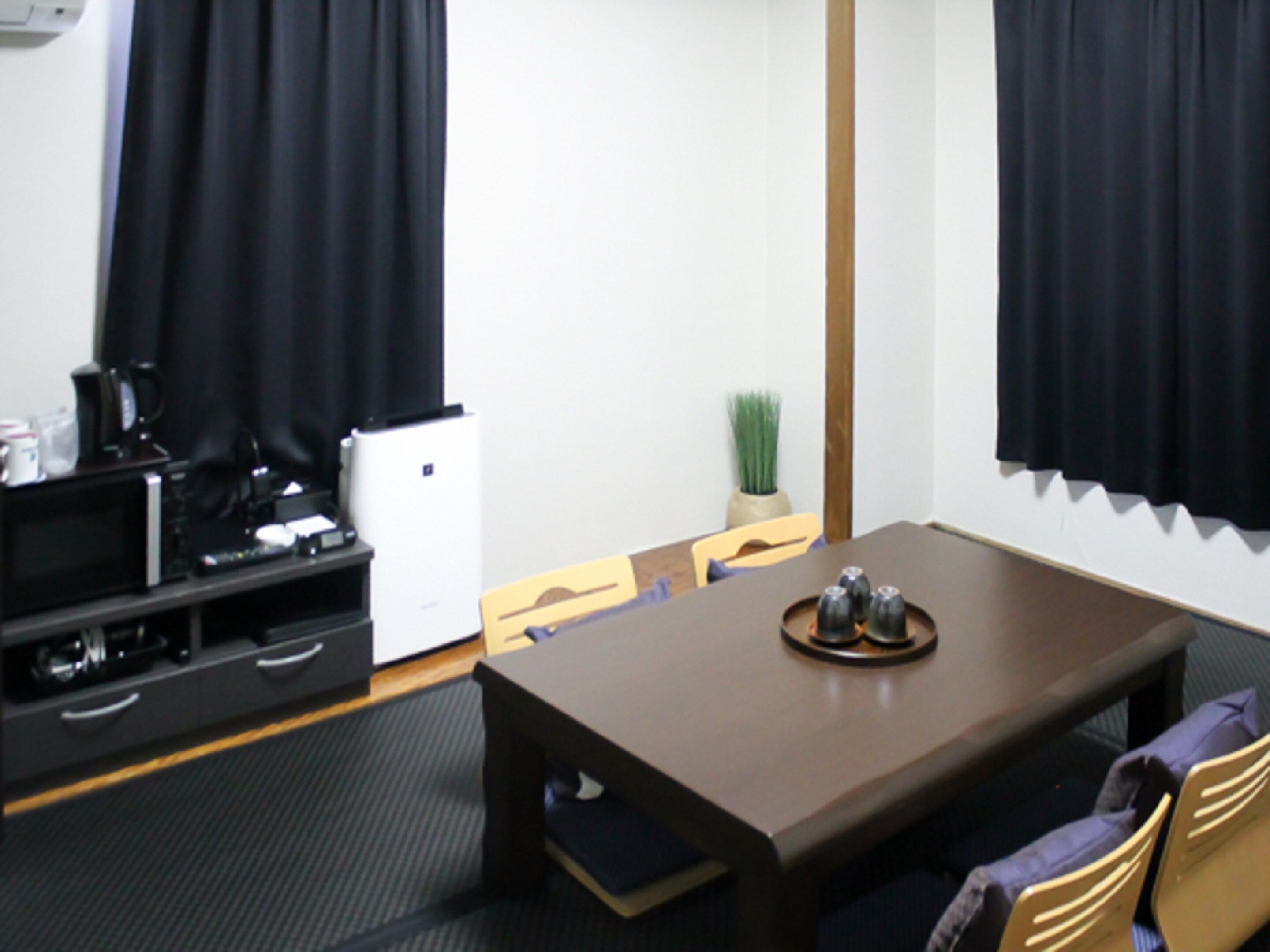 Una habitación de hotel compacta con una mesa de comedor de madera, un refrigerador pequeño, un microondas y un televisor sobre un pedestal.