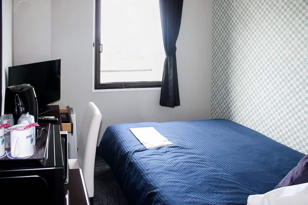Una habitación de hotel con una cama, un escritorio con computadora, un televisor y una ventana con cortinas.