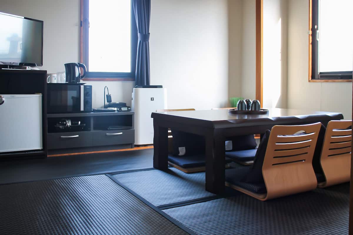 Habitación de hotel compacta con kitchenette, comedor con mesa y sillas, televisión y ventana con cortinas.
