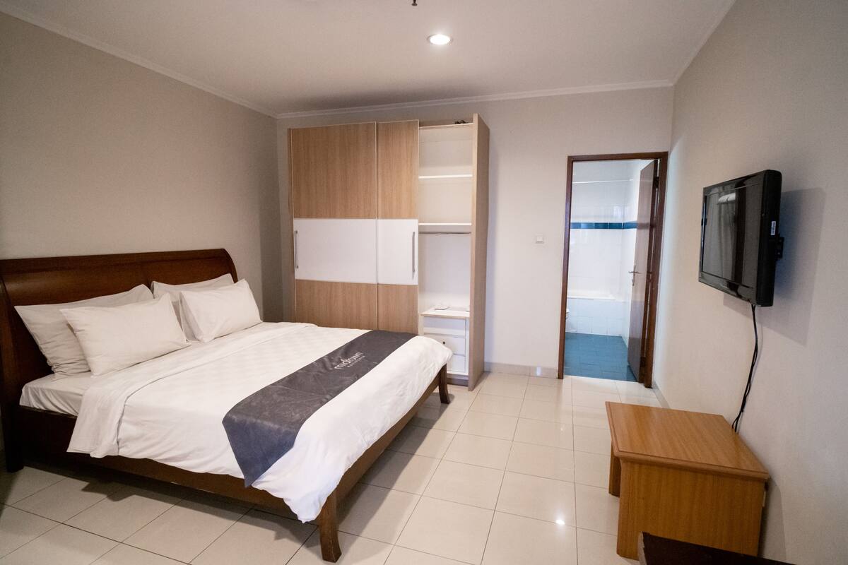 Een hotelkamer met een houten bed, een kledingkast, een televisietoestel en een klein houten tafeltje.