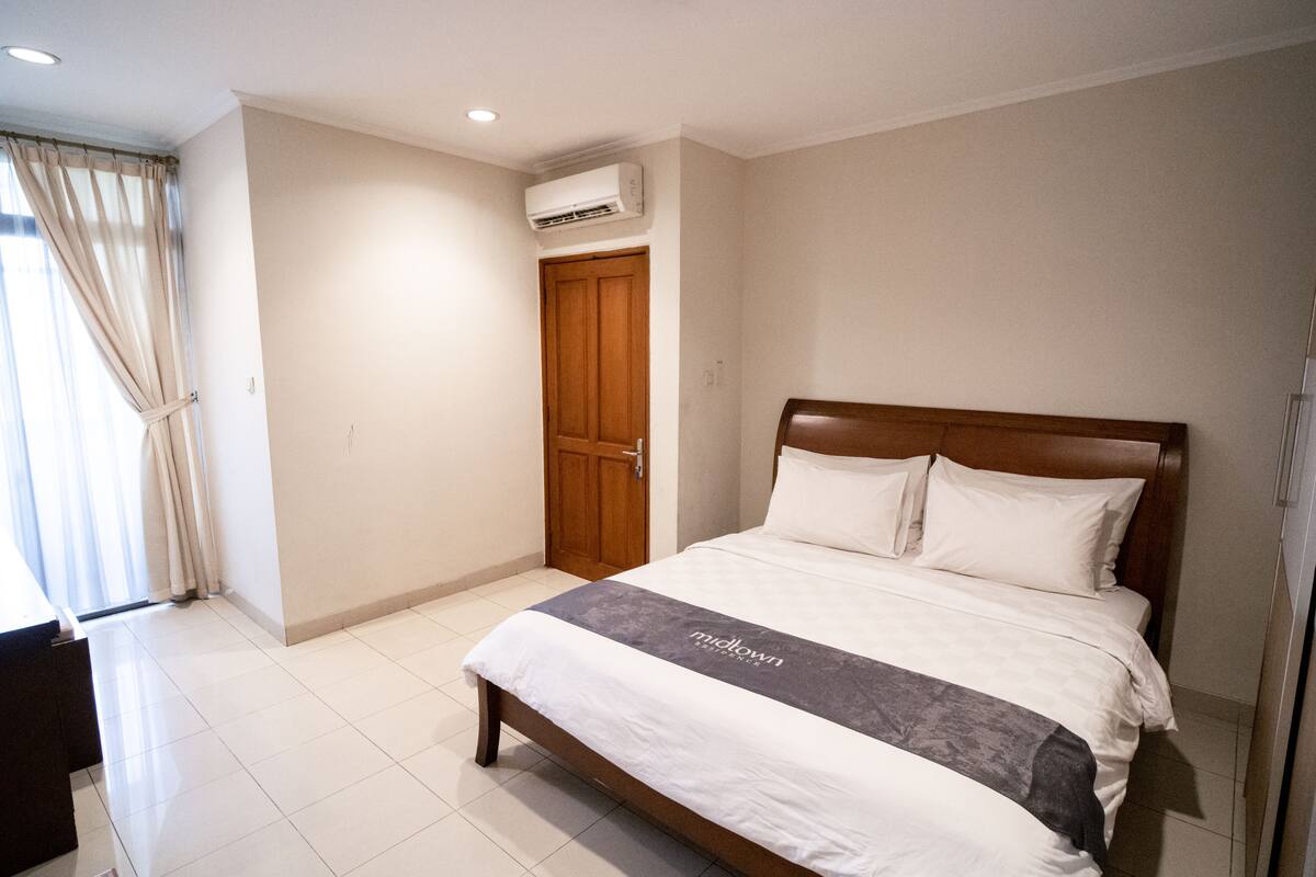 A hotel room with a large bed, a wooden headboard, a bedside table, and a window with curtains.