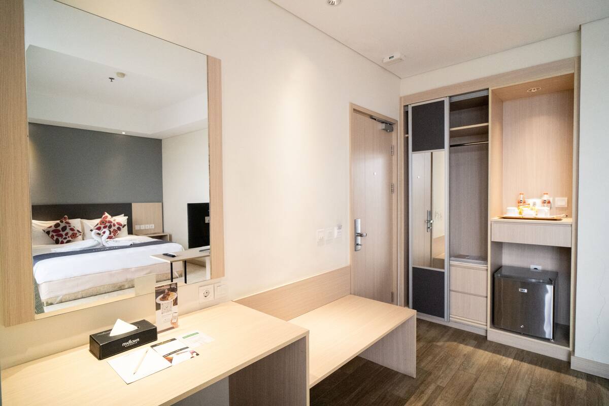A modern hotel room with a bed, a desk, a mirror, a wardrobe, and a walk-in closet.