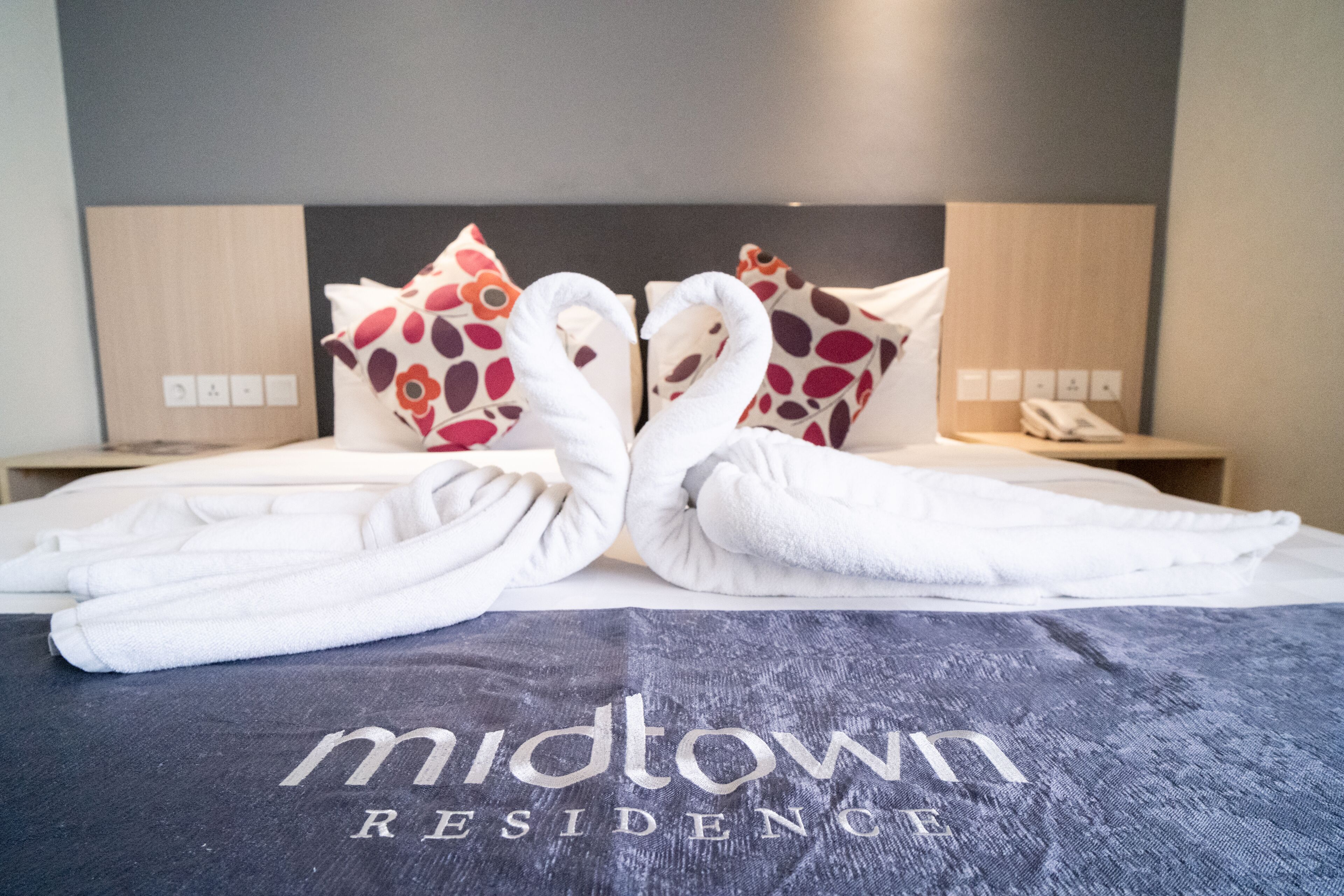 Een bed met handdoeken gevouwen in de vorm van zwanen, een sprei met de tekst 'midtown residence' en een houten hoofdbord.