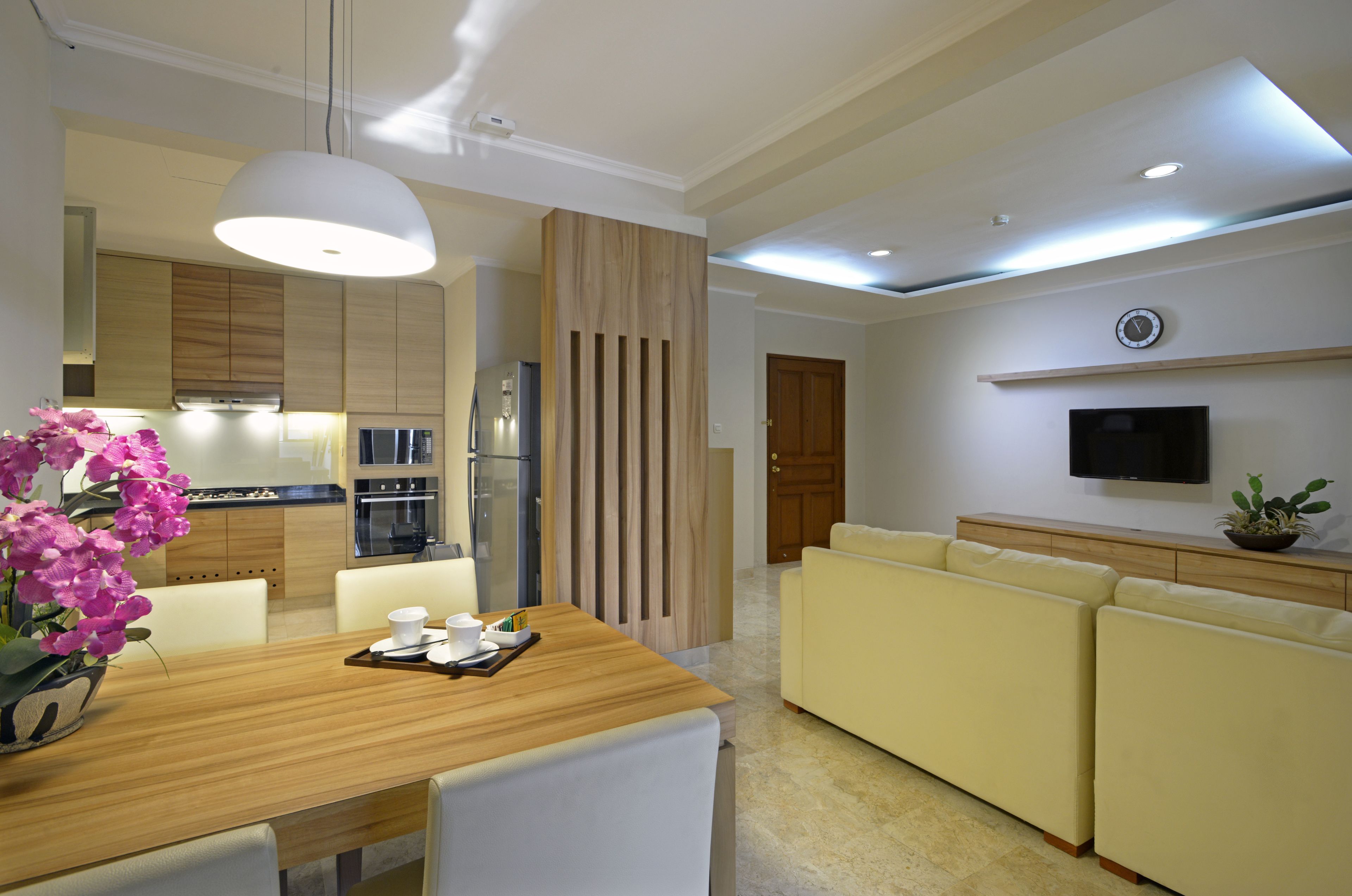 A modern living room with a wooden dining table, yellow sofas, and a flat-screen TV mounted on the wall.