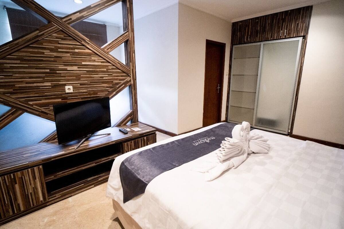 A hotel room with a bed, a TV on a wooden console, a large mirror, and a wardrobe.