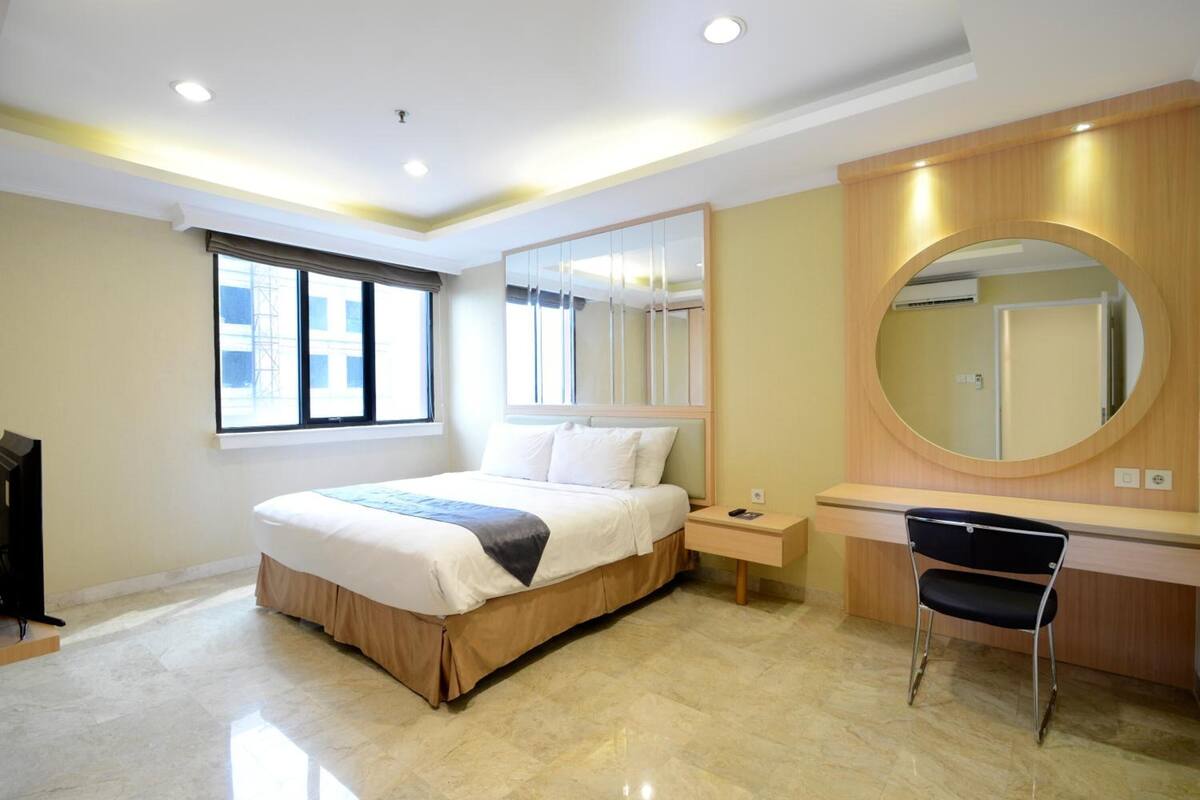 A modern hotel room with a large bed, bedside table, chair, and a large mirror.