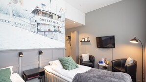A hotel room with a bed, a desk, a chair, a TV, and a wall-mounted artwork. - Hotell Leksand (Leksand)