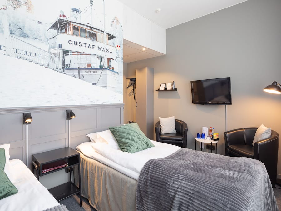 A hotel room with a bed, a desk, a chair, a TV, and a wall-mounted artwork.