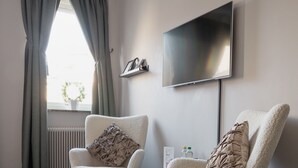 A modern living room with two plush armchairs, a small table, a flat-screen TV, and a window with curtains. - Hotell Leksand (Leksand)