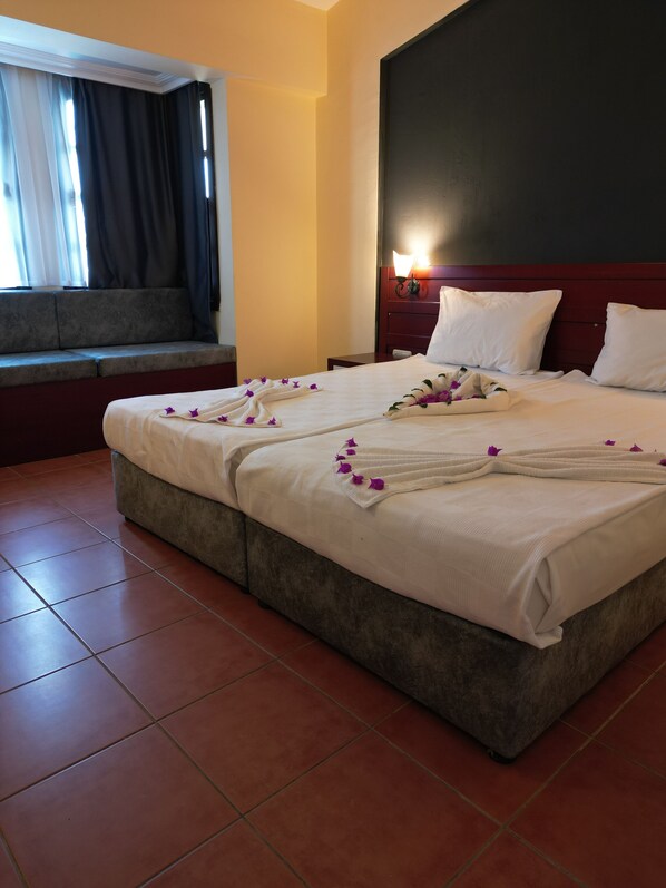 Une chambre d’hôtel avec un grand lit, une table de chevet, une commode, une fenêtre avec des rideaux et une lampe fixée au mur.